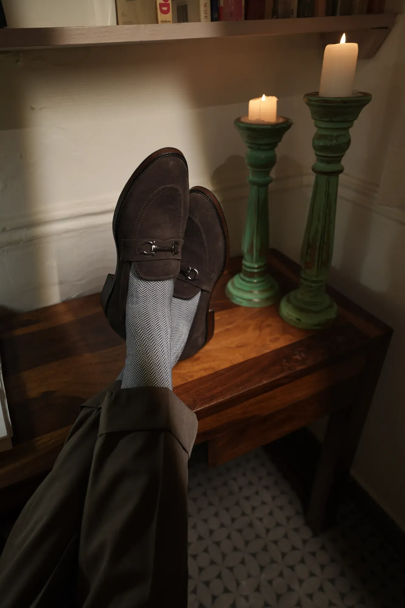 Loafers resting on a walnut side table beside two candles