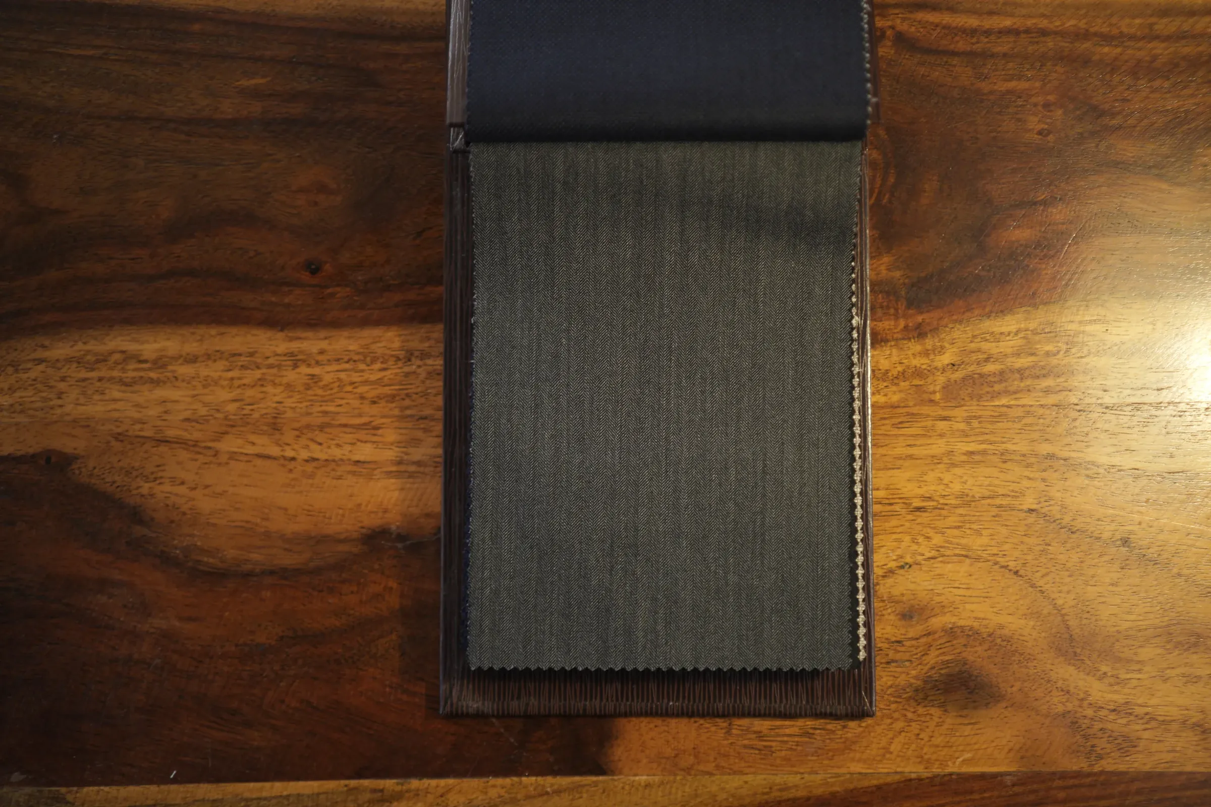 A book of suiting cloth open on a walnut table